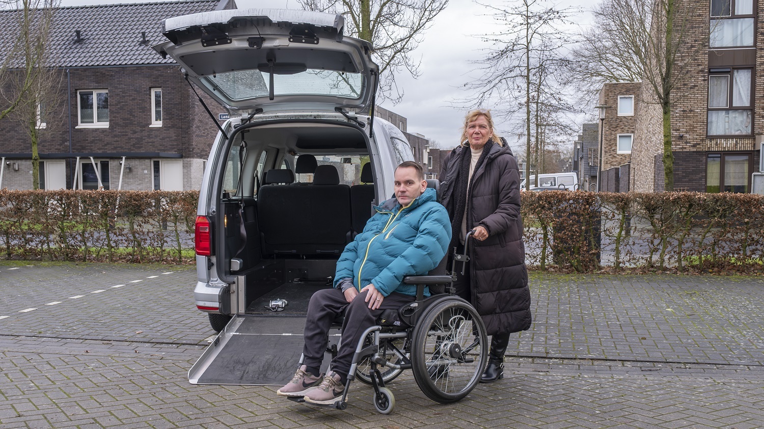 Ramon zit in een rolstoel. Hij en zijn moeder Tonny staan voor rolstoelauto VERA. De klep van de auto staat open. Ramon kan de auto in rijden.