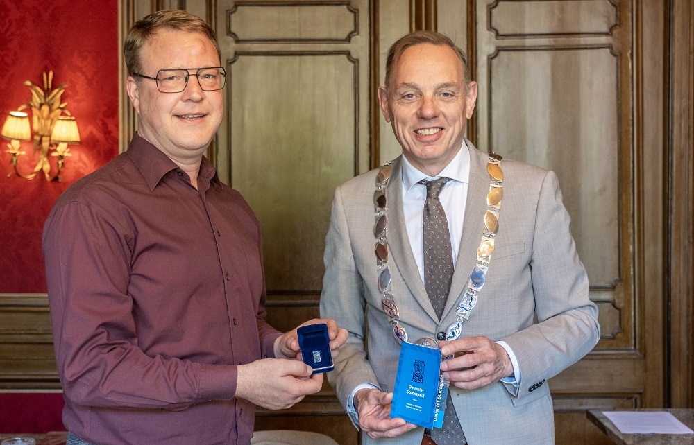 Karst Vaartjes en burgemeester Ron König staan naast elkaar. Vaartjes houdt de Deventer Stadsspeld die hij net heeft ontvangen.